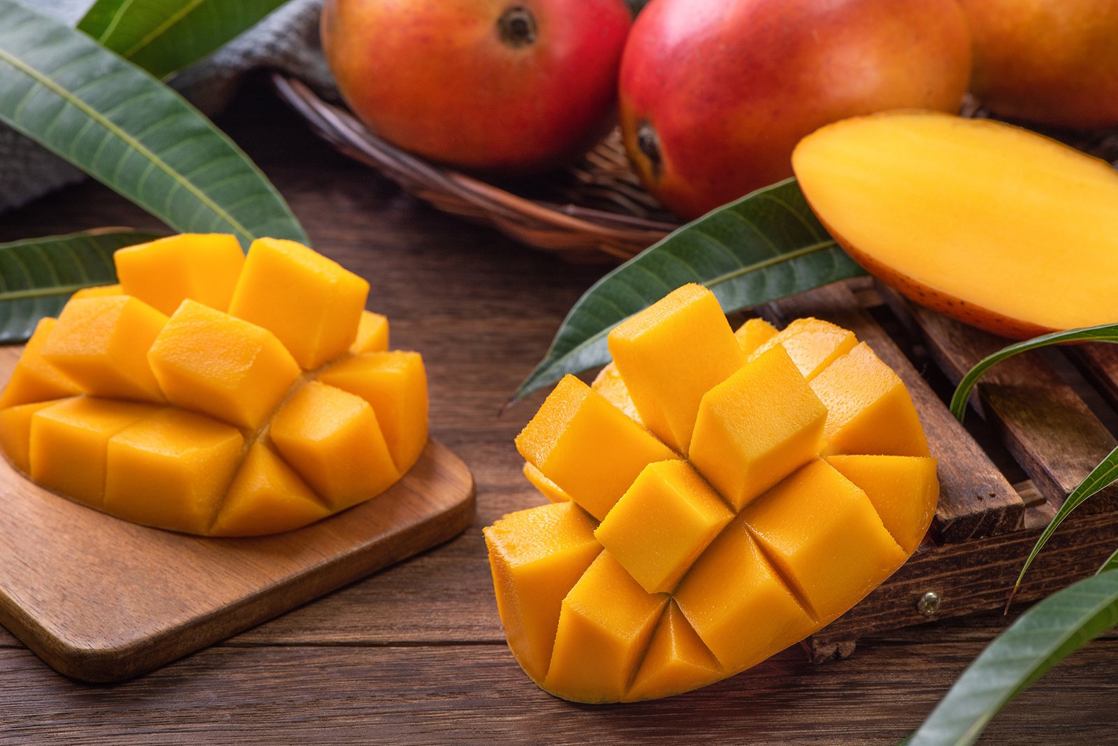 Mango. Close up of fresh ripe mango fruit with leaves over dark wooden table background with green leaves.